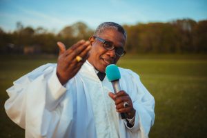 Priest in Glasses Holding a Microphone and Gesturing